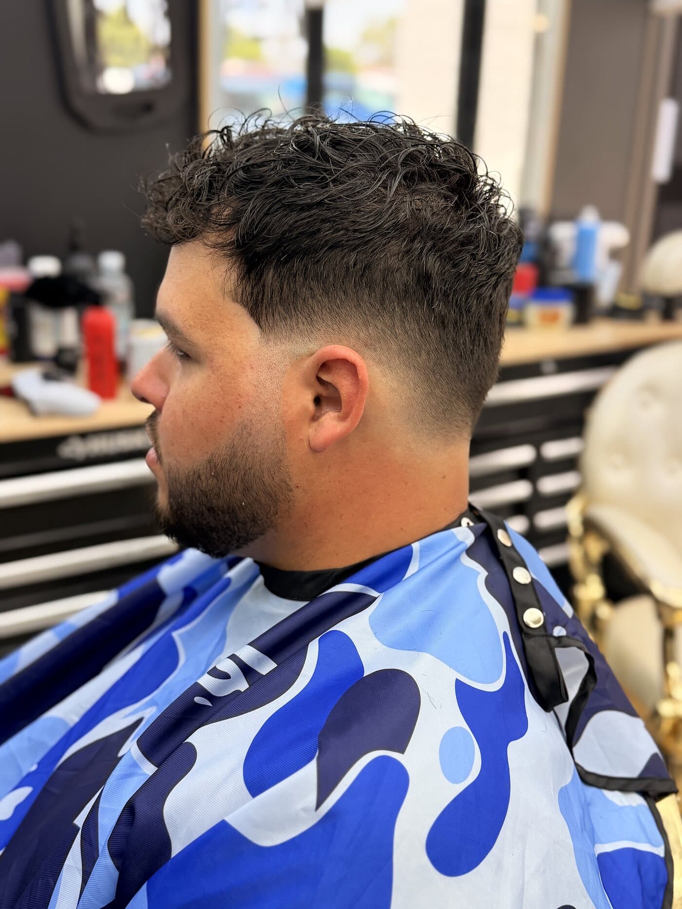 Curly top over a mid fade with a shaped beard